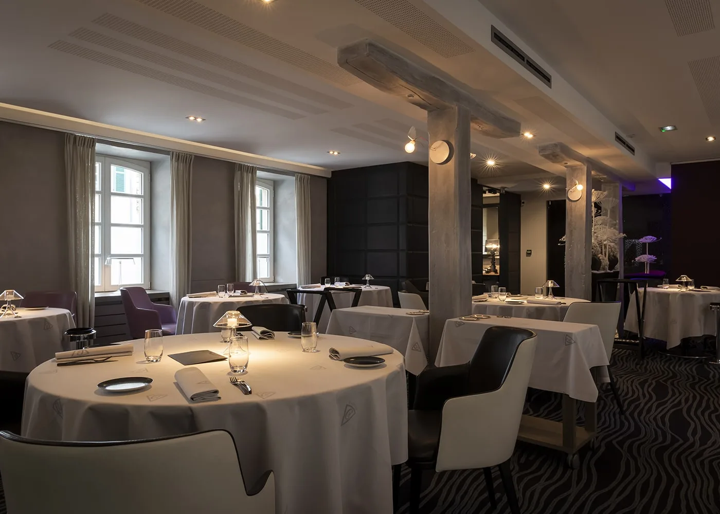 Salle du restaurant Il Cortile : tables rondes nappées de blanc entre des poteaux de bois patiné, sous un éclairage chaud.