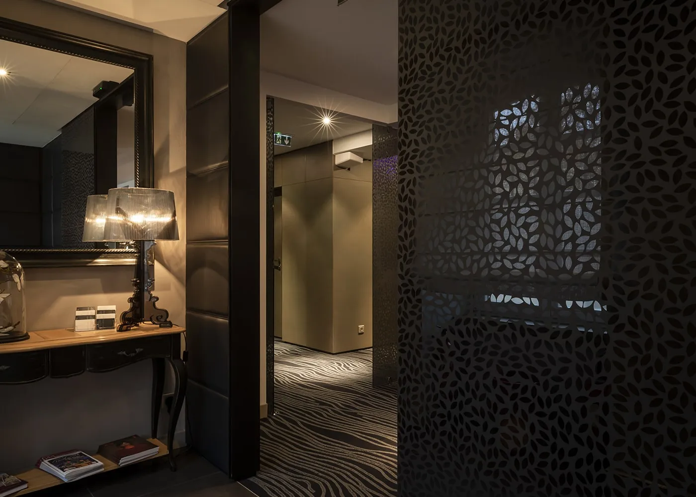 Entrée du restaurant : miroir ancien, lampe sur console et cloison métallique ajourée à motif de feuilles.