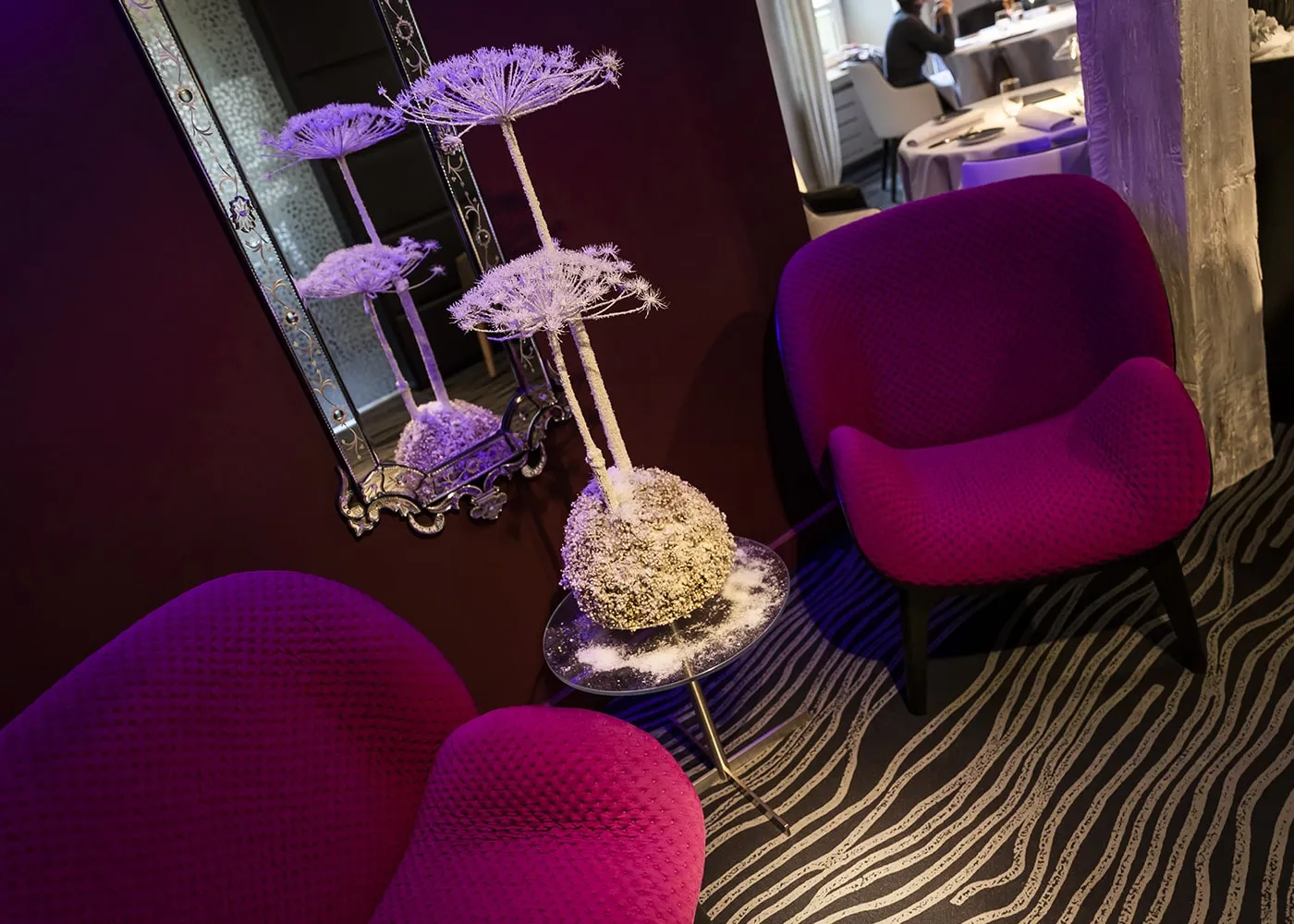 Salon d’attente : fauteuils fuchsia, miroir vénitien et éclairage indirect violet.