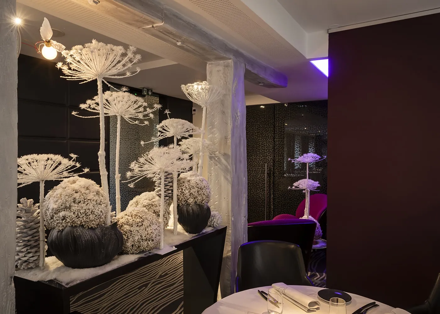 Détail du salon : fauteuils fuchsia, guéridon et tapis zébré sous une lumière violette.