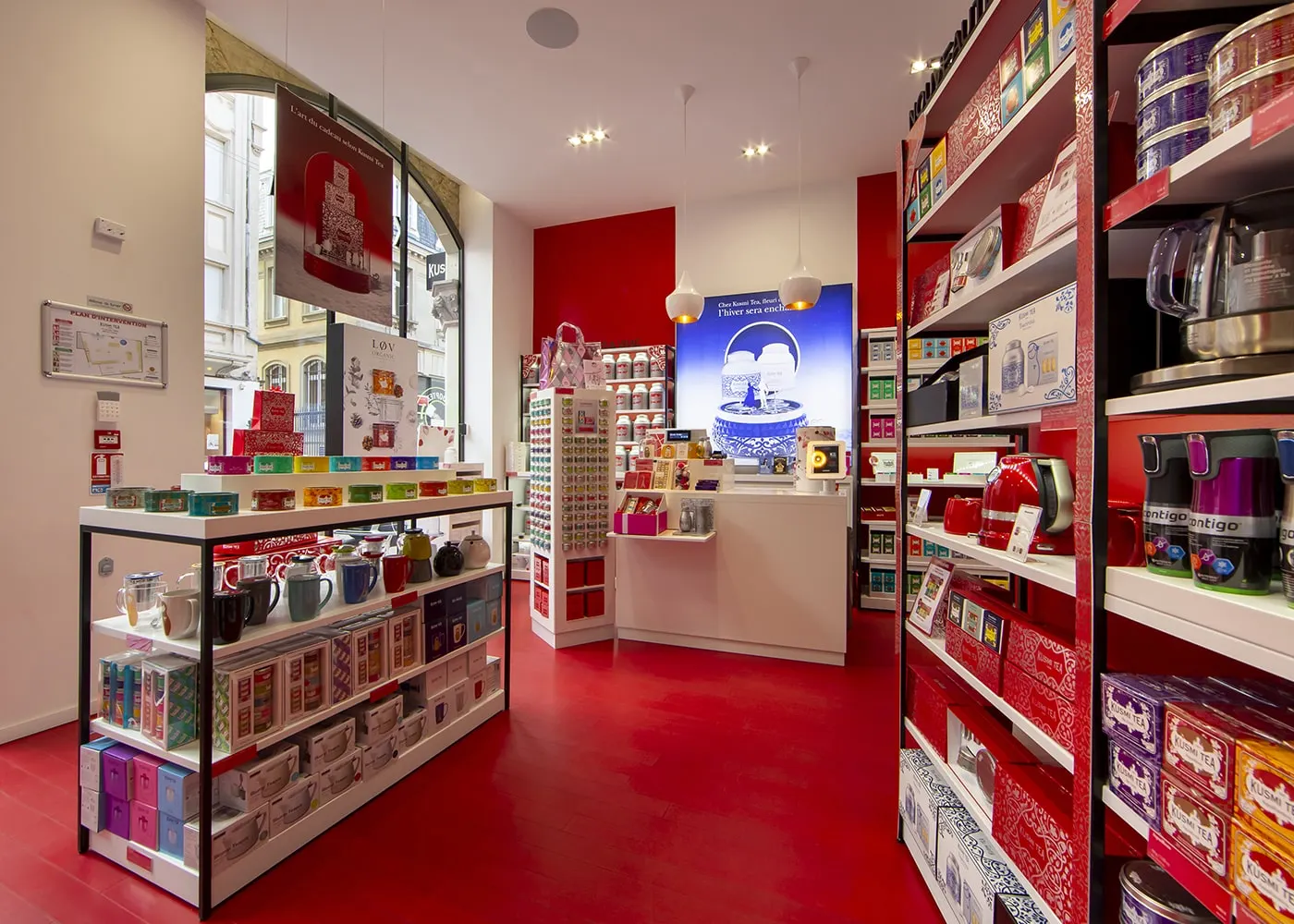 Perspective vers le comptoir : présentoirs blancs, murs rouges et suspensions en porcelaine.