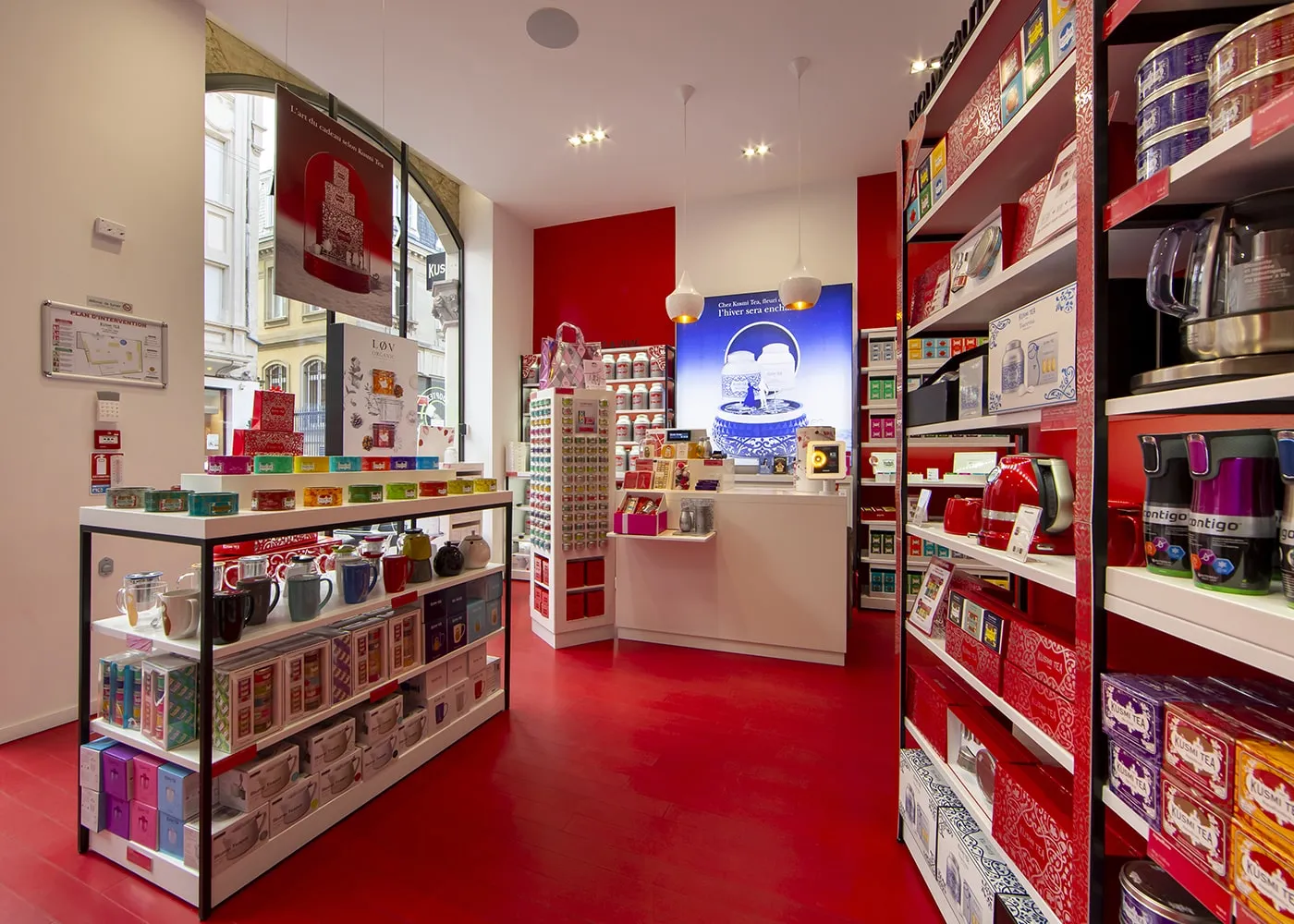 Perspective vers le comptoir : présentoirs blancs, murs rouges et suspensions en porcelaine.