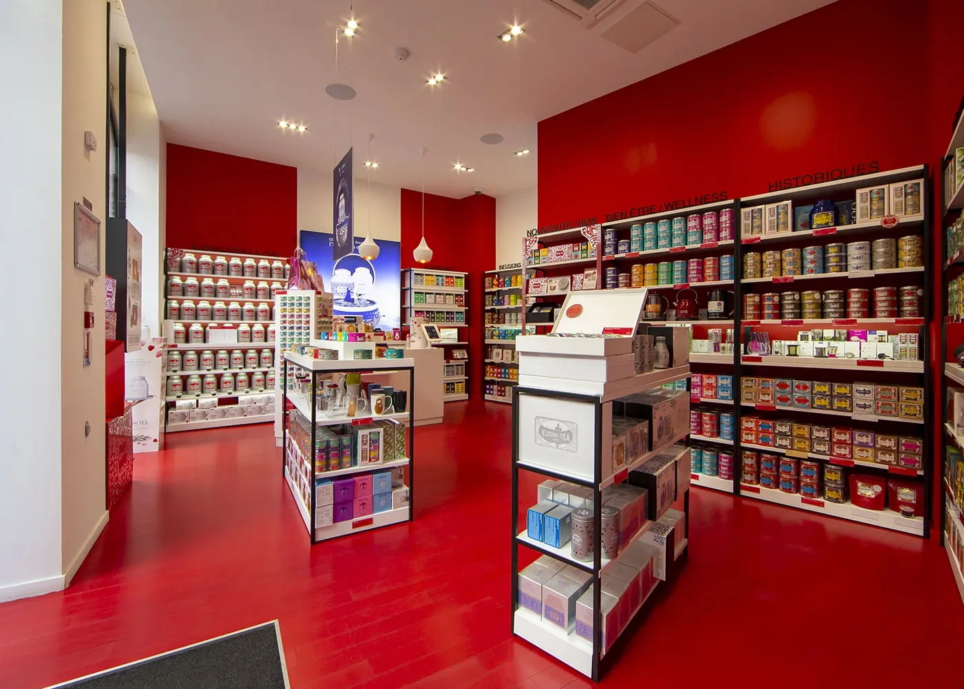 Vue large de la surface de vente, rayonnages de boîtes de thé sur toute la hauteur du mur rouge.