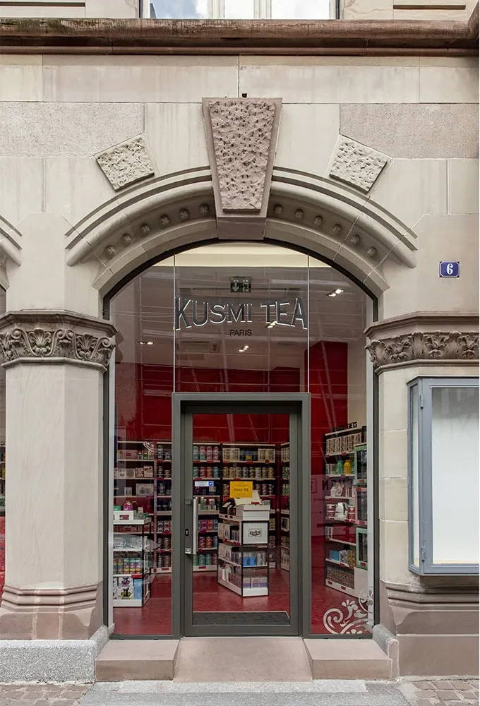 Façade de face : arche de pierre sculptée, vitrine vitrée et intérieur rouge visible depuis la rue.